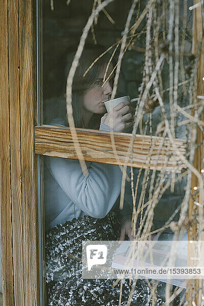 Woman drinking tea behind window pane