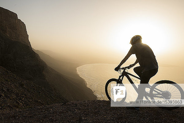 Spain  Lanzarote  mountainbiker on a trip at the coast at sunset enjoying the view
