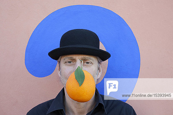 Portrait of man with an orange at a wall with question mark wearing a bowler hat