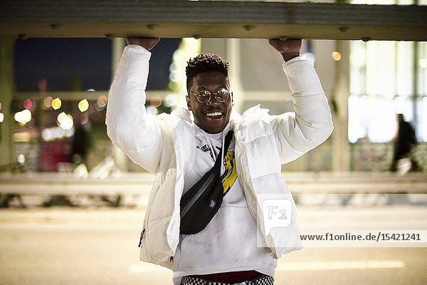 Young smiling man doing pull-ups on metal construction of bridge Hackerbrücke Hacker bridge at night in city next to street in Munich Germany