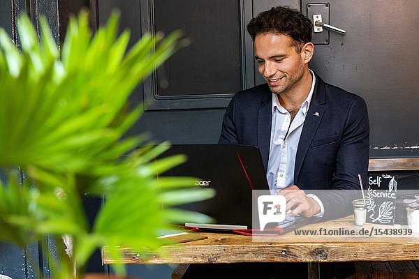 Berlin Germany. Young Adult & Gay Professional working with his laptop computer and smartphone inside a coffee place to help out his customers with their online marketing and seo.
