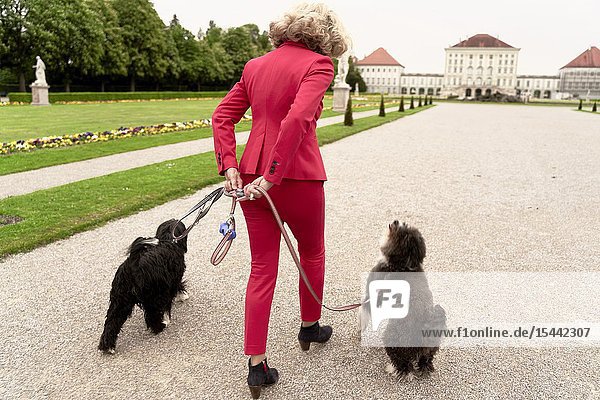 Senior woman (67 years old) walking with two dogs in park in Nymphenburg Munich Germany.