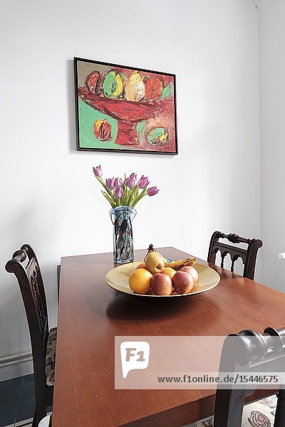 Kitchen dining table with three empty chairs fruit bowl and still-life painting on the wall Berlin Germany.