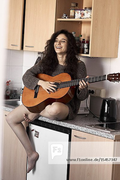 Young woman playing guitar in kitchen at home