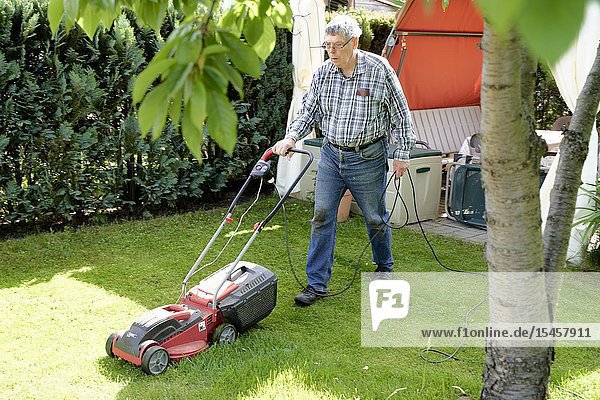 Senior man mowing lawn in garden with electric lawnmower