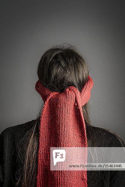 Girl with dark long hair blindfolded with a red knitted scarf- back view.