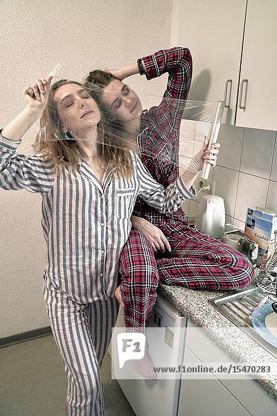 Two young women behind plastic foil in kitchen wearing pyjamas