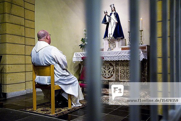 Hulsberg Netherlands. Catholic priest father and pastor praying the rosary in front of a Mother Mary Statue inside his rural village church.