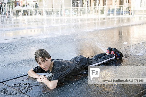 Tilburg  Netherlands. Teenage boy playing with fountain water during the hot summer and the annual carnival and fair.