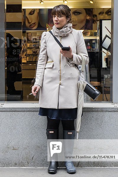 New York City New York USA. Young attractive and fashionable woman smoking her hourly cigarette just outside the shop and store she is working. Smoking tobacco products inside workplaces is nog longer allowed toe prevent other from inhaling unhealthy chemicals.