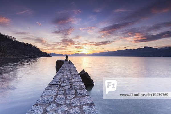 A lonely man staring at a colorful winter sunset at the old pier  Lake Maggiore  Ispra  Varese Province  Lombardy  Italy.