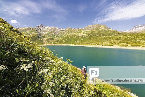 Hikers with baby in backpack on shore of Lake Montespluga Chiavenna Valley Sondrio province Valtellina Lombardy Italy.