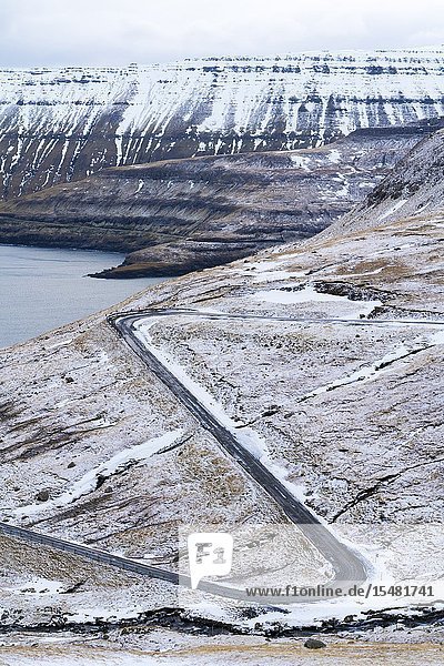 Winding road on mountains towards the ocean Funningur Eysturoy island Faroe Islands Denmark.