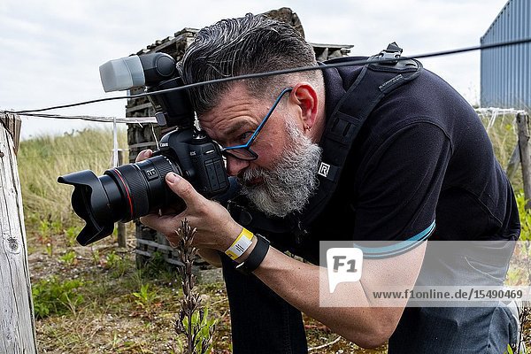 Oostvoorne Netherlands. Hipster Man with Beard and Huge Camera making a photograph as a semi professional photographer.