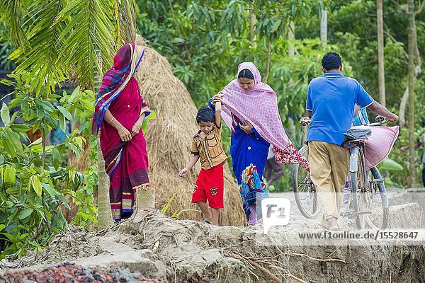 Bangladesh - June 27 2015: Man woman and peoples are crossing river erosion affected roadside at Rasulpur Barisal District.