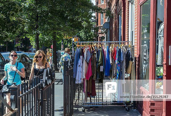 People walk past a rack of clothing outside an apparel store in the Greenpoint neighborhood of Brooklyn on Sunday June 9 2019. (© Richard B. Levine).