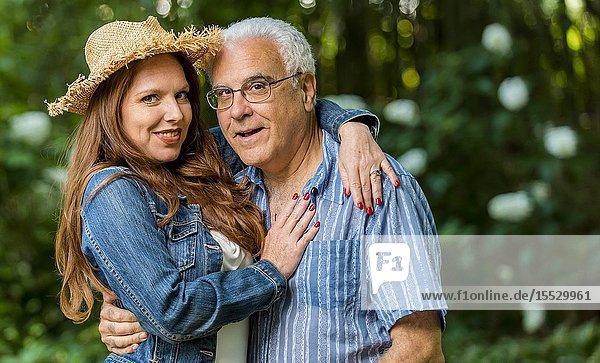 A 40 Year old readheaded woman and a 66 year old man smiling at the camera  outdoors.