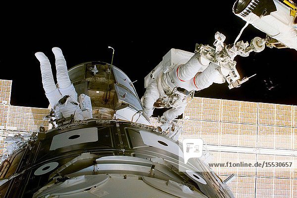 Astronauts James H. Newman (left) and Jerry L. Ross work between Zarya and Unity (foreground) during the first of three scheduled spacewalks on the STS-88 mission. Newman is tethered to the module while Ross is anchored at the feet to a mobile foot restraint mounted on the end of the remote manipulator system (RMS) arm.