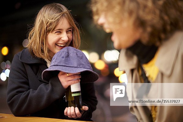 Happy woman hiding bottle of wine alcohol under hat at night thrill of anticipation nightlife in Berlin Germany
