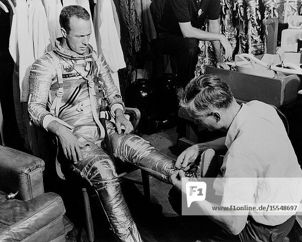 Mercury astronaut M. Scott Carpenter prime pilot for the Mercury-Atlas 7 (MA-7) spaceflight and Crew Equipment Specialist Joe Schmidt are pictured during a suiting exercise. Schmidt is seen lacing up Carpenter's boots.