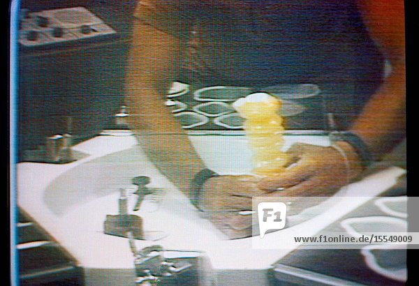 An accordian-style beverage dispenser filled with orange juice is held by astronaut Charles Conrad Jr. Skylab 2 commander in this close-up view which is a reproduction taken from a color television transmission made by a TV camera aboard the Skylab 1 2 space station cluster in Earth orbit. Conrad (head and face not in view) is seated at the wardroom table in the crew quarters of the Orbital Workshop. The dispenser contained beverage crystals and Conrad has just added the prescribed amount of water to make the orange drink.