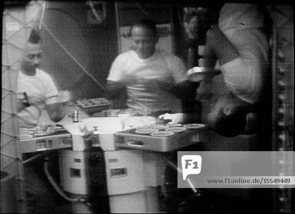 The three Skylab 3 crewmen are shown eating in the Orbital Workshop (OWS) wardroom of the Skylab space station in Earth orbit in this photographic reproduction taken from a television transmission made by a color TV camera aboard the OWS. Astronaut Alan L. Bean (right) commander illustrates eating under zero-gravity conditions upsidedown. The two other crewmen are scientist-astronaut Owen K. Garriott (left) science pilot and astronaut Jack R. Lousma pilot.