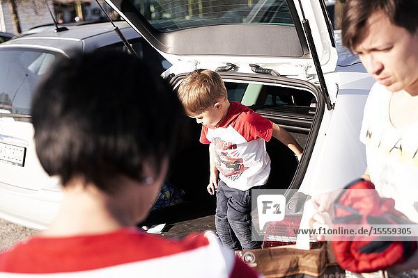 Toddler child jumping out of car boot next to parents