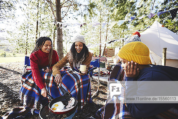 Lesbisches Paar und Kinder kochen Frühstück am Grill auf dem Campingplatz im Wald