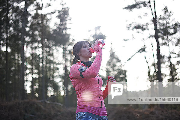 Läuferin trinkt im Wald aus einer Wasserflasche