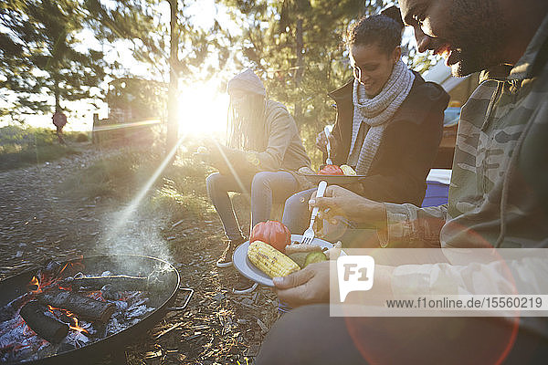 Familie beim Essen am sonnigen Lagerfeuer auf dem Campingplatz im Wald