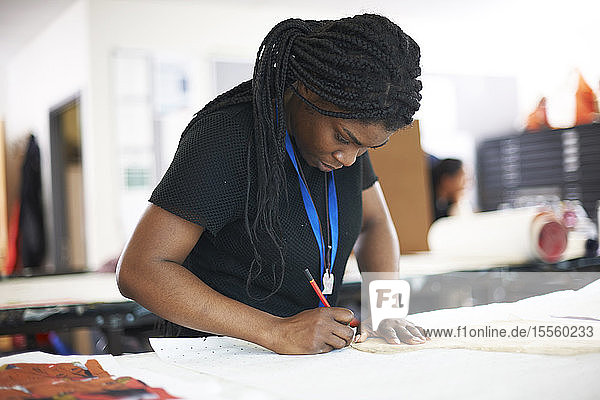 Fokussierte Modedesignerin beim Nachzeichnen eines Nähmusters im Atelier
