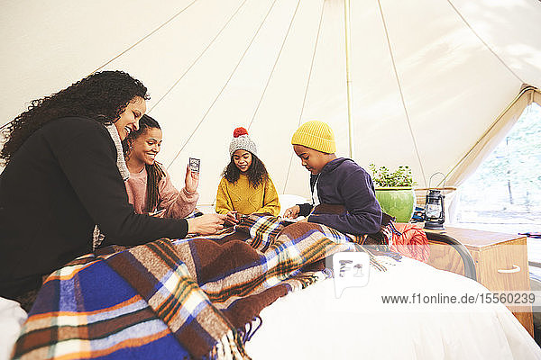 Lesbisches Paar und Kinder spielen Karten auf dem Bett in einer Camping-Jurte