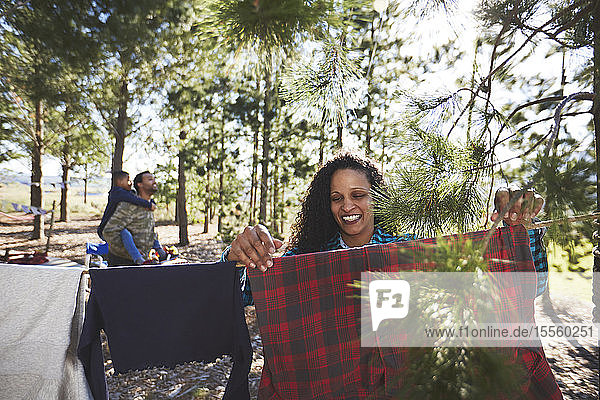 Lächelnde Frau  die Kleidung an einer Wäscheleine auf dem Campingplatz im Wald aufhängt