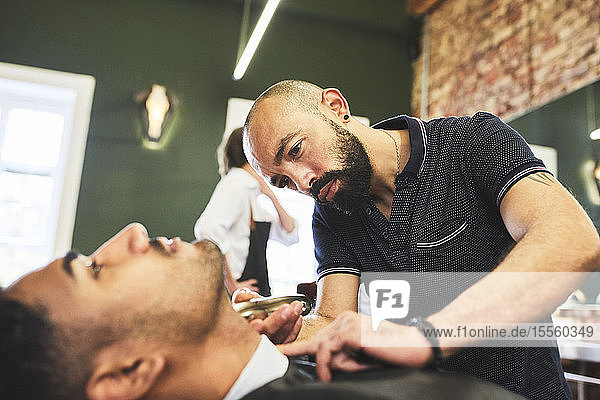 Focused male barber giving customer a shave in barbershop