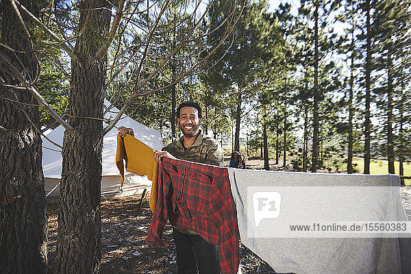 Porträt glücklicher Mann hängt Wäsche auf Campingplatz Wäscheleine n Wald
