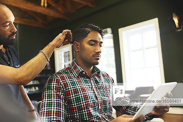Mann benutzt digitales Tablet beim Haarschnitt im Friseursalon
