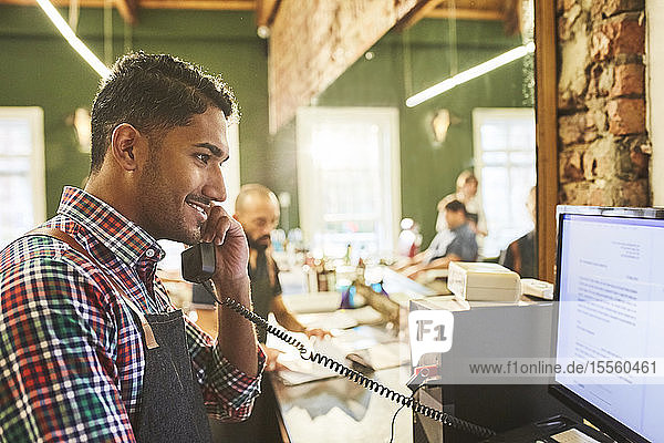 Male barber talking on telephone at computer in barbershop