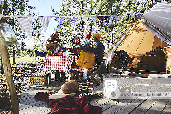 Lesbisches Paar und Kinder essen am Picknicktisch vor der Jurte auf einem sonnigen Campingplatz