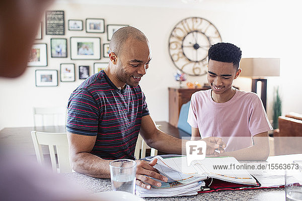 Father helping teenage son with homework in kitchen