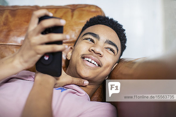 Smiling teenage boy using smart phone on sofa