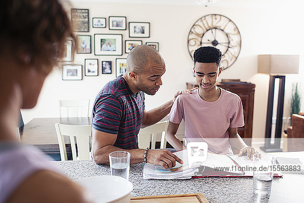 Father helping teenage son with homework in kitchen