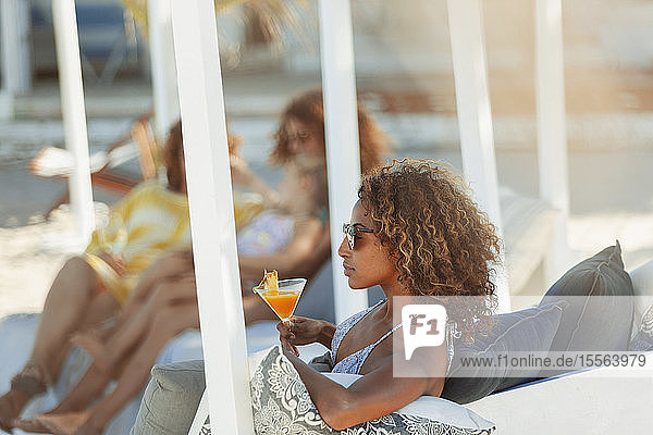 Junge Frau entspannt sich mit einem Cocktail auf einer Strandterrasse