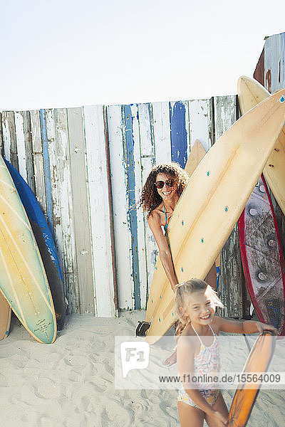 Portrait happy mother and daughter with surfboard on sunny beach