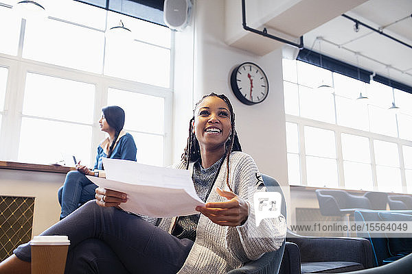 Glückliche  selbstbewusste Geschäftsfrau mit Papierkram im Büro