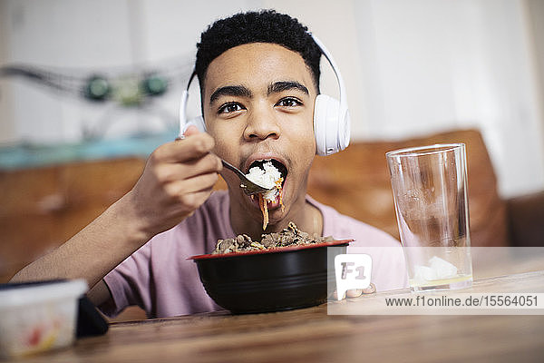 Portrait teenage boy with headphones eating at coffee table