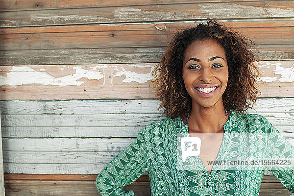 Porträt einer glücklichen  zuversichtlichen jungen Frau vor einer Holzplankenwand