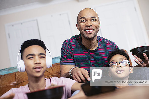 Smiling father and sons eating and watching TV
