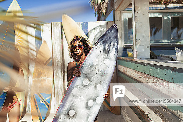 Portrait junge Frau mit Surfbrett am sonnigen Strand
