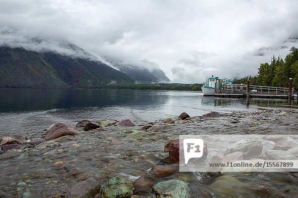 A tourist boat docks along the rocky shoreline at Lake McDonald in Glacier National Park.