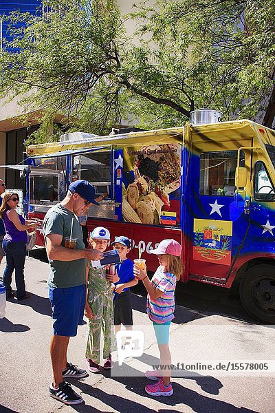 Father with his three children texting his location at a Venezuelan food trcuk at the Tucson Meet Yourself Folk Festival.